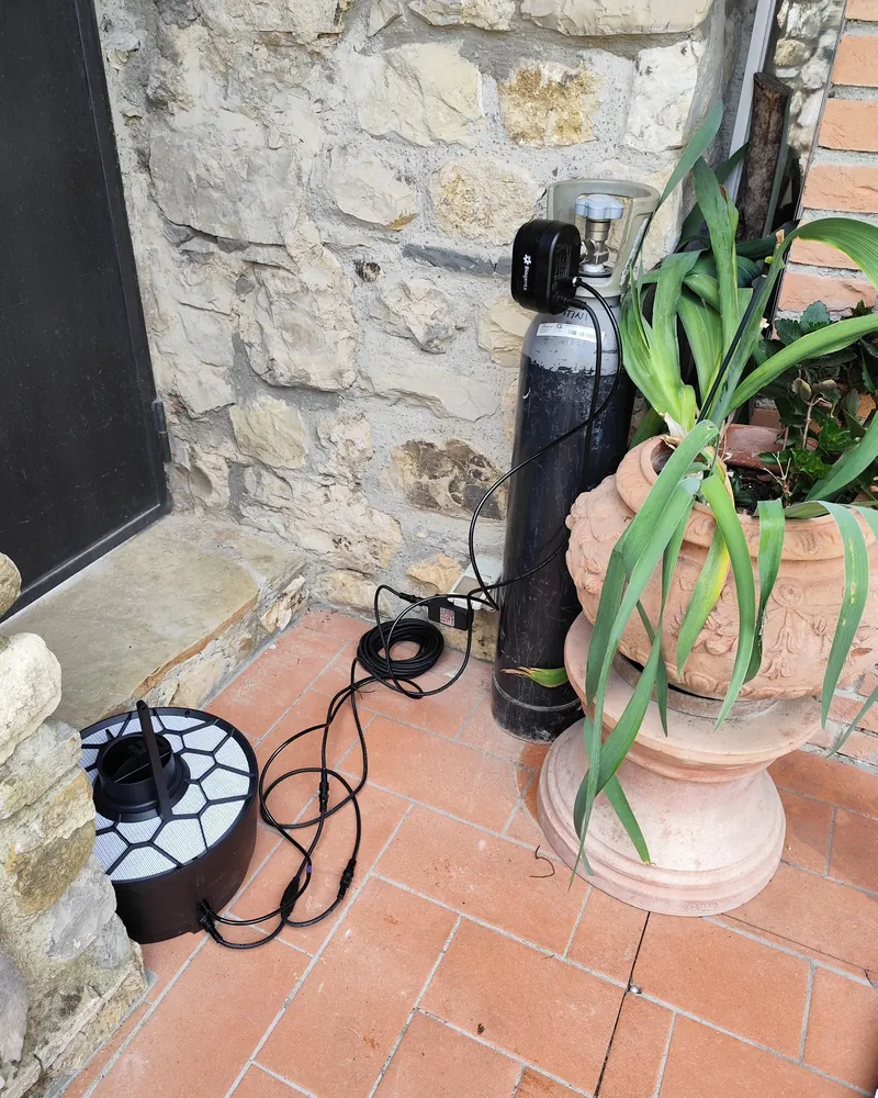 Trappola antizanzare a CO₂ collegata alla sua bombola, accanto a un muro in pietra e a un vaso