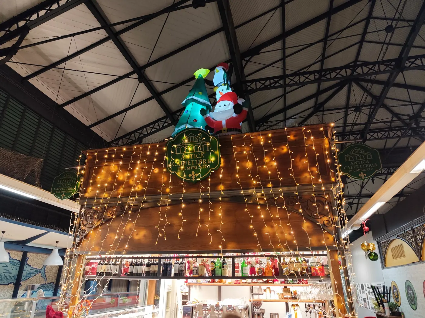 Bancone di una caffetteria in un mercato coperto con tende di luci calde e Babbo Natale, pupazzo di neve e albero gonfiabili illuminati in cima