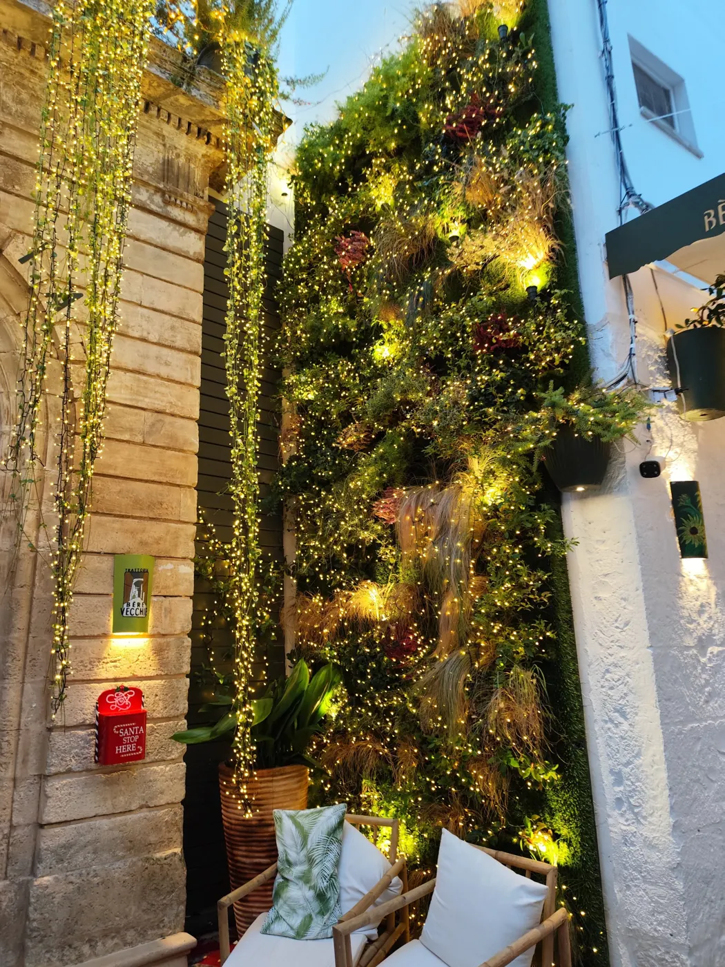 Parete verde illuminata con luci bianco caldo e cascate di luci sulla facciata in pietra di una trattoria
